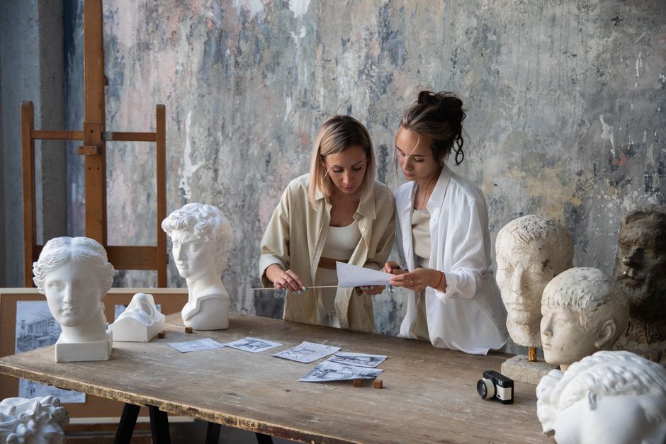 Two women artists examining gypsum heads and drawings in an art workshop.