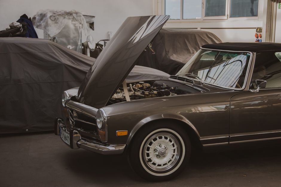 Classic Mercedes car in a garage with its hood open, showcasing the engine.